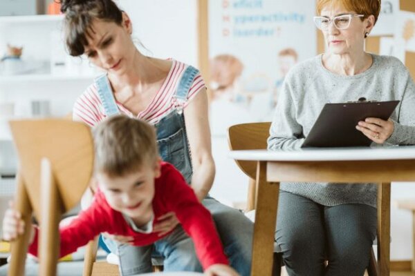 Kid crawling under the table during therapy for ADHD with his mother and professional therapist